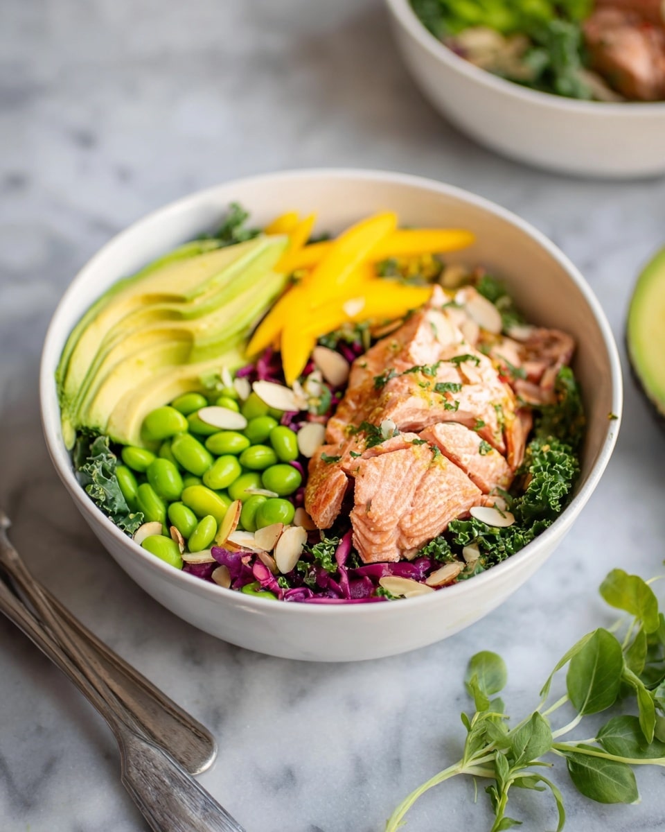 The dish shows a white bowl filled with several layers starting at the bottom with mixed greens that include slices of kale and purple cabbage. On top of the greens are bright green edamame beans placed on one side, next to thinly sliced yellow mango, and near the front are slices of ripe avocado showing creamy light green color. There are also pieces of cooked salmon with a light pinkish-orange color, sprinkled with herbs, placed on the right side. Scattered almond slivers are visible over the salad parts, adding texture contrast. The bowl rests on a white marbled surface, with some greenery near the bottom right and a metal fork nearby. Photo taken with an iphone --ar 4:5 --v 7