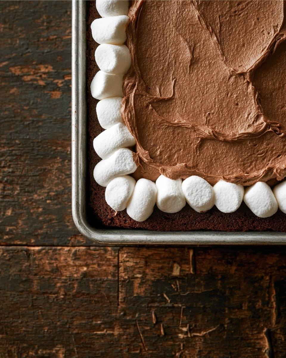 A close-up view of a rectangular chocolate dessert in a metal tray featuring three layers: the bottom layer is a dark brown, soft-looking cake base, above it is a row of fluffy, white marshmallows neatly lined along the edge, and the top layer is a thick, creamy chocolate spread with a smooth, slightly textured surface, partly covering the marshmallows. The tray sits on a dark wooden surface with visible grain and marks. photo taken with an iphone --ar 4:5 --v 7