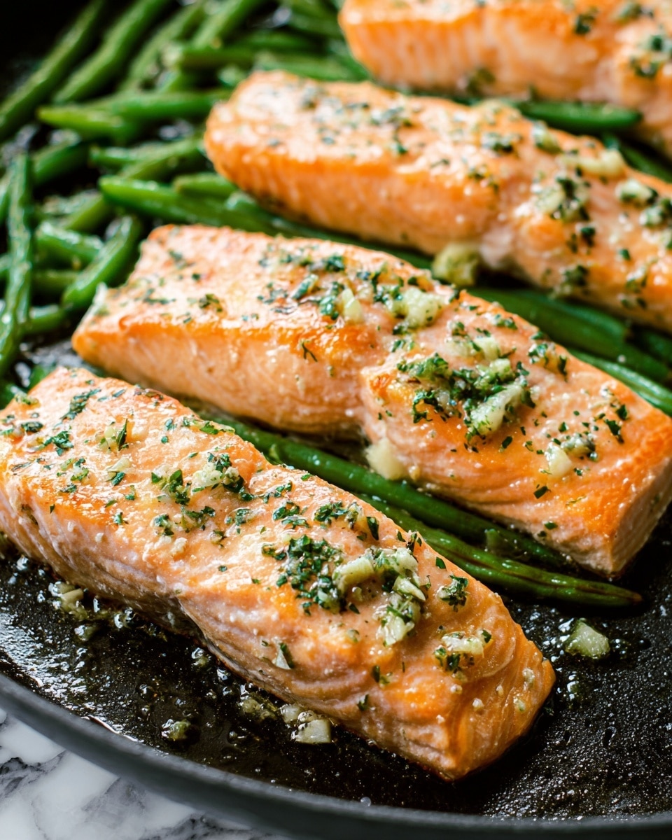 Several light orange salmon fillets are placed on a black pan, resting on a bed of cut green beans. The salmon pieces are cooked with a slightly golden, shiny surface, sprinkled with finely chopped green herbs and small pieces of garlic. The green beans underneath add contrast with their fresh green color and slightly cooked texture. The background is a white marbled texture. photo taken with an iphone --ar 4:5 --v 7