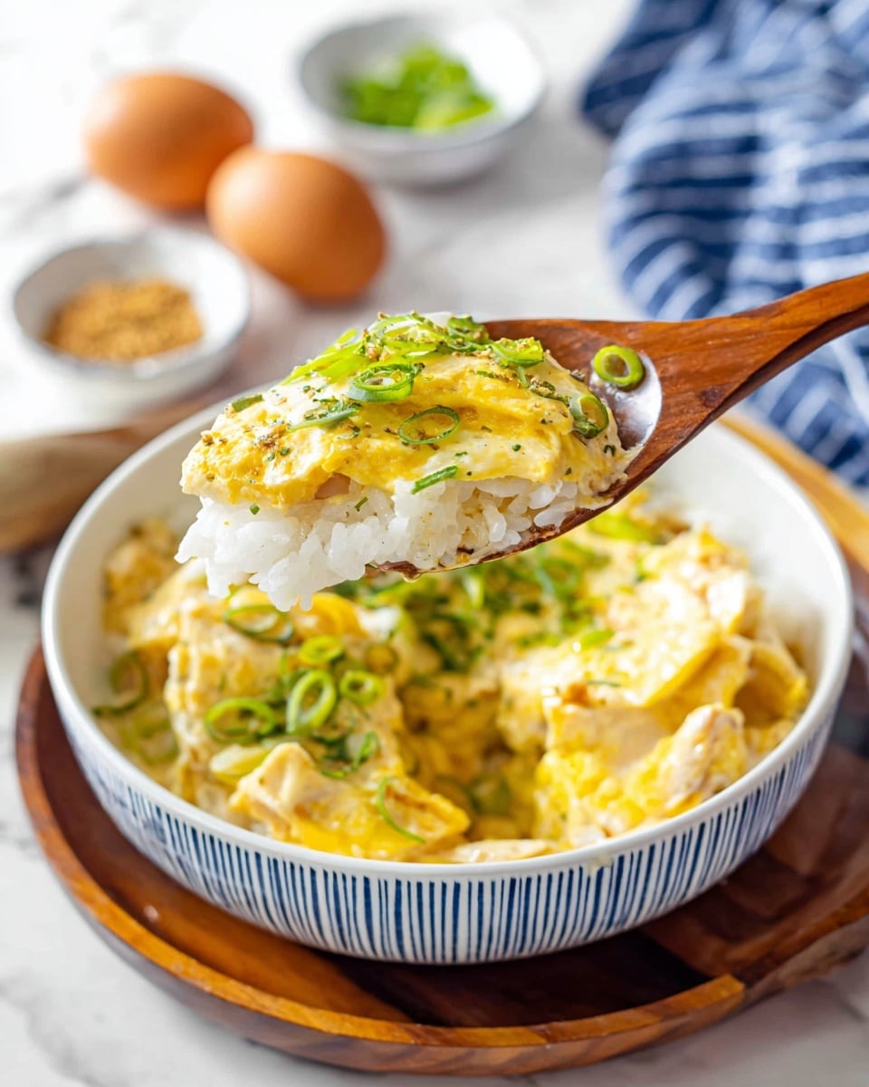 A close-up view of a wooden spoon holding a layered bite of white rice at the bottom, topped with tender pieces of light yellow chicken, soft yellow cooked egg, and garnished with bright green sliced scallions, lifted above a white bowl with blue stripes filled with the same dish. The bowl sits on a dark wooden tray placed on a white marbled surface. In the background, there are three brown eggs on a blue and white striped cloth and small white bowls with light brown seasoning and green chopped herbs. The dish looks warm and creamy with a mix of smooth and slightly textured layers, fresh green highlights, and a cozy, inviting feel. Photo taken with an iphone --ar 4:5 --v 7