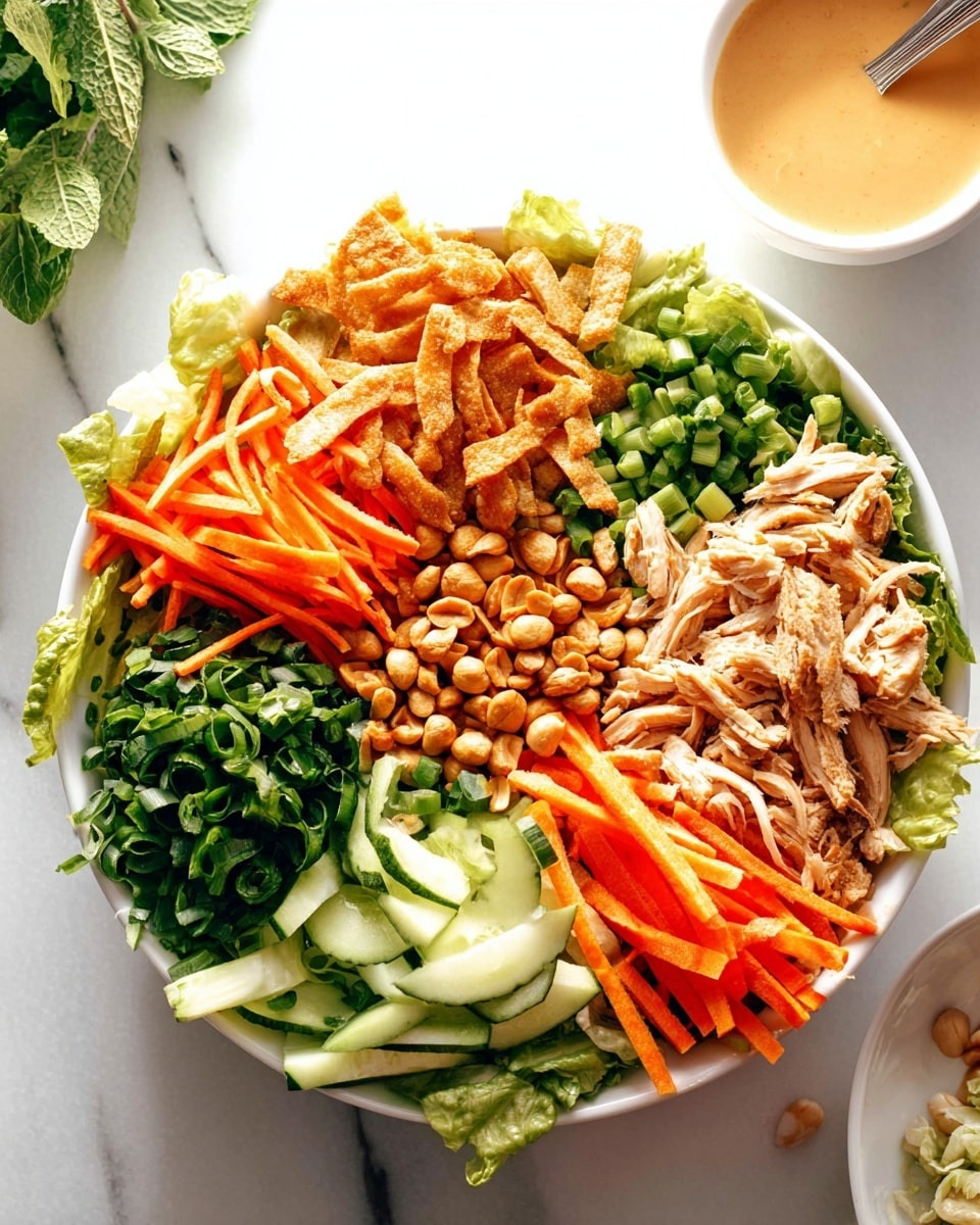This is a white bowl filled with layers of fresh ingredients arranged in sections. Starting from the top right are crispy golden fried strips, below those are light brown roasted peanuts, then light orange carrot sticks, and shredded light brown chicken pieces. Moving counterclockwise, there is green lettuce, chopped green onions, bright green leafy herbs, and thin dark green cucumber sticks. To the top right of the bowl is a white bowl with a creamy light brown sauce, with a spoon in it. The background and surface are white marble. photo taken with an iphone --ar 4:5 --v 7
