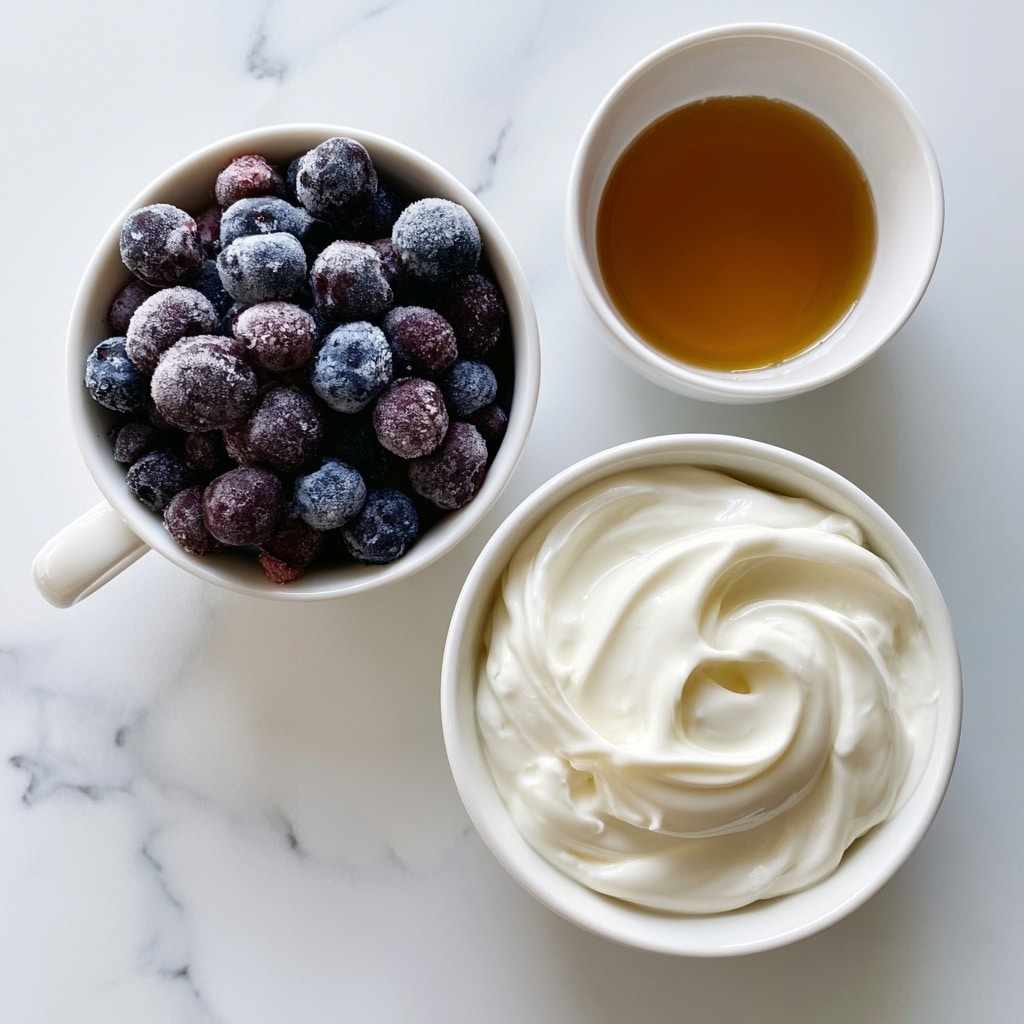 A top view of three white bowls on a white marbled surface. The first bowl, with a small handle, is filled with small, round frozen blueberries covered in ice crystals, showing dark purple and blue colors. The second bowl holds thick, creamy white Greek yogurt with a smooth texture and soft swirls on the surface. The third, smallest bowl contains golden-brown maple syrup with a glossy shine. Each bowl is clearly labeled with black text on white background boxes: