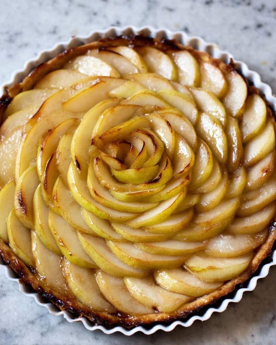 A round tart with multiple layers of pear slices arranged in a circular pattern, starting from the outer edge and moving inward. The pear slices are light yellow with areas of brown caramelized edges, giving a slightly shiny texture. The layers overlap and form a rose-like shape in the center. The tart sits inside a white fluted tart pan on a white marbled surface. Photo taken with an iphone --ar 4:5 --v 7
