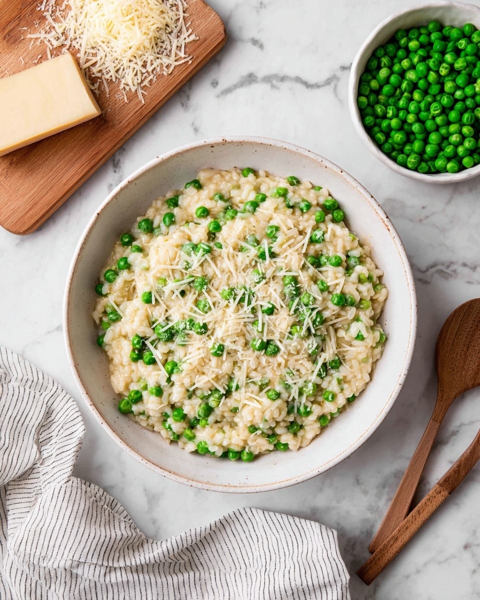 A white bowl filled with creamy risotto mixed with bright green peas scattered evenly throughout. The risotto is pale beige with a soft, smooth texture, and small bits of chopped green herbs are sprinkled on top. There is a silver spoon partially stirring the risotto, showing the rich, slightly sticky consistency of the rice. The bowl sits on a white marbled surface, providing a clean, light background. photo taken with an iphone --ar 4:5 --v 7