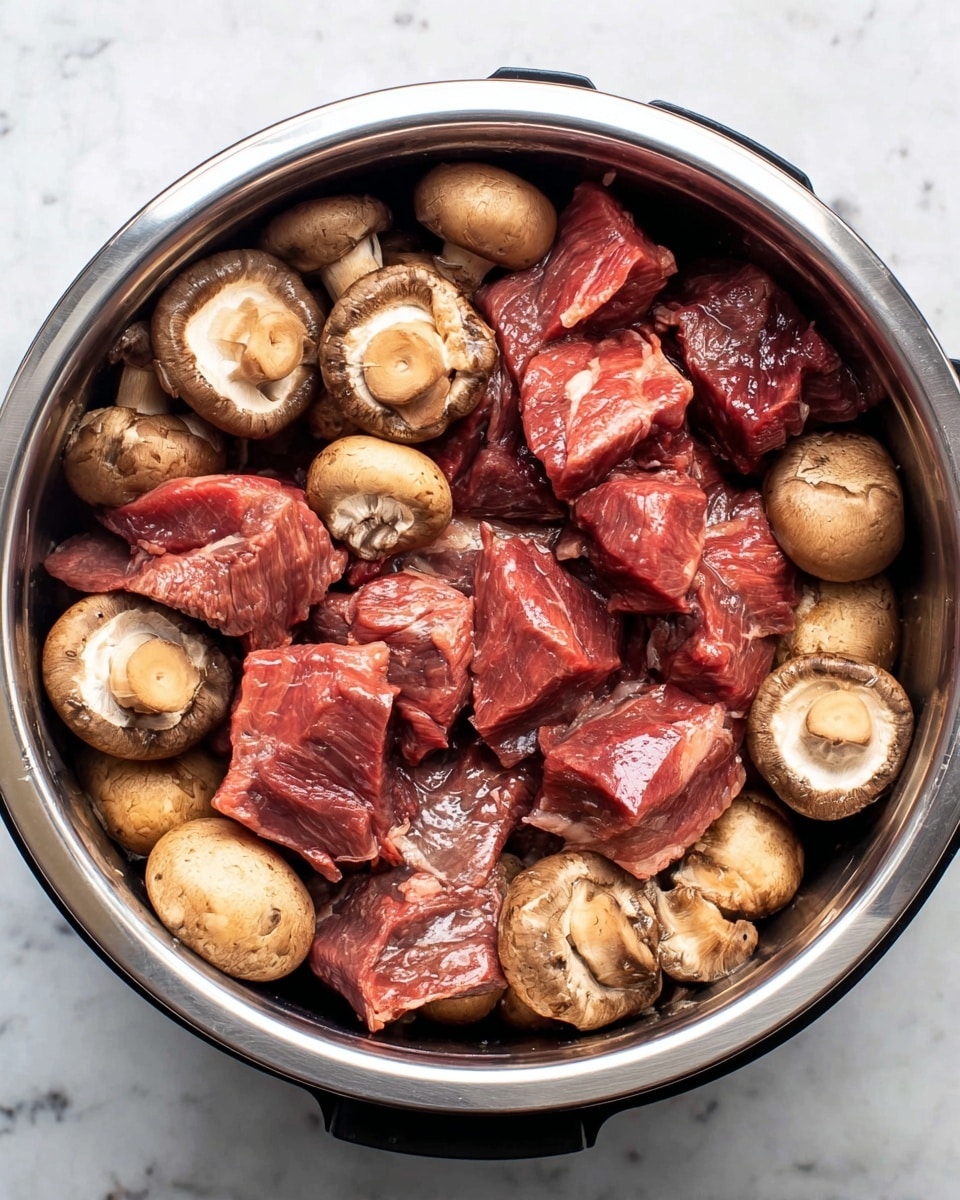Inside a round silver cooking pot on a white marbled surface, there are two layers mixed together: the bottom layer partially visible is made of whole, smooth, beige-brown mushrooms with a slightly shiny wet texture, and the top layer consists of large, thick chunks of raw beef with a deep reddish-pink color, some pieces showing glistening fat and muscle texture; the beef and mushrooms are arranged evenly throughout the pot, showing a mix of both elements. photo taken with an iphone --ar 4:5 --v 7