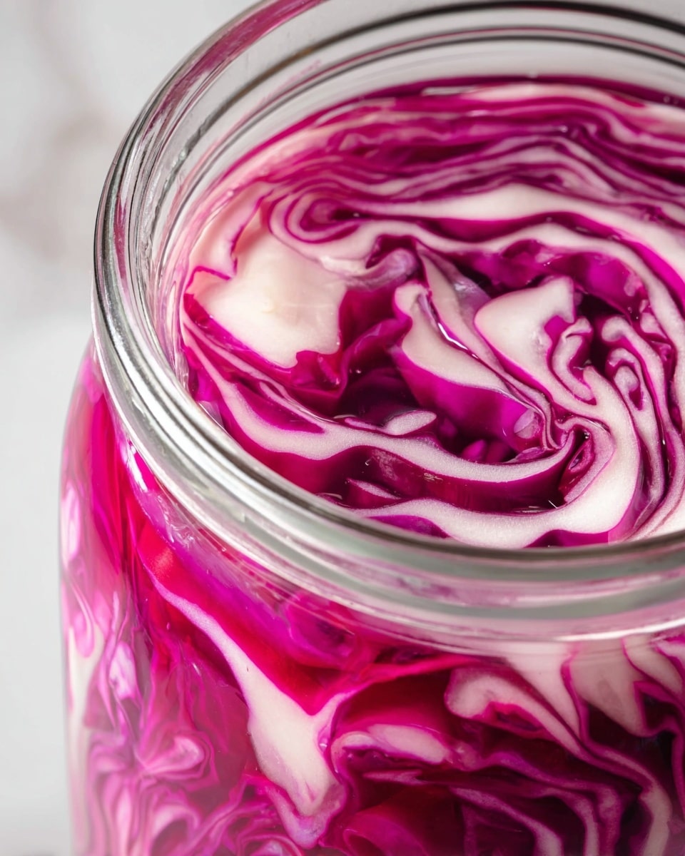 A close-up of thinly sliced layers of bright pink and white cabbage tightly packed inside a clear glass jar, submerged in a clear, slightly bubbly liquid. The cabbage slices show crisp texture with curving edges and contrasting colors of deep magenta and pale white creating a vibrant visual pattern at the top of the jar. The jar rim is visible with smooth, clear glass, and the background is a white marbled texture. photo taken with an iphone --ar 4:5 --v 7