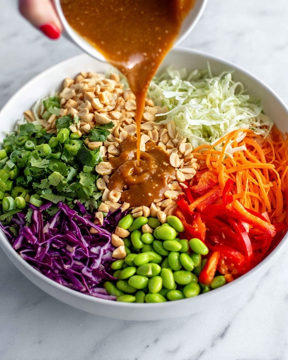 A white bowl on a white marbled surface holds seven colorful layers: shredded white cabbage with chopped peanuts in the top left, bright green sliced scallions in the top right, chopped green edamame in the bottom right, shredded orange carrots next to the scallions, fresh green cilantro with peanuts in the center, thin red bell pepper strips with peanuts on the bottom left, and shredded purple cabbage with peanuts between the white cabbage and cilantro. A woman's hand with red nail polish pours a thick brown dressing over the cilantro center, creating a small pool on top of it. Photo taken with an iphone --ar 4:5 --v 7