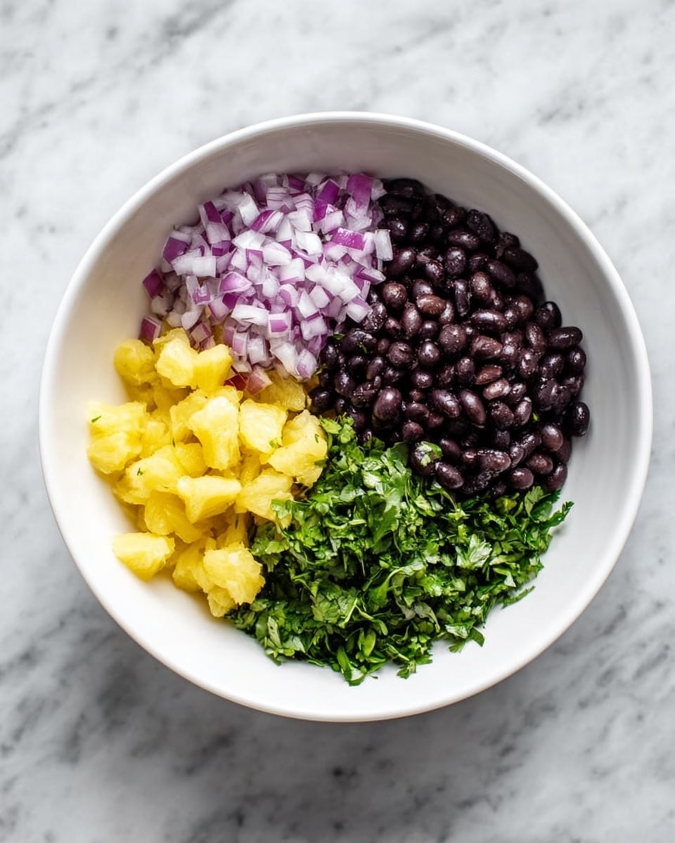 A white bowl sits on a white marbled surface, holding four separate layers of ingredients arranged side by side. On the top left is finely chopped purple onion with a crisp texture. To its right is small yellow pineapple pieces with a juicy and slightly translucent look. Below the onion is a layer of whole, shiny black beans with a smooth texture. Finally, to the right of the beans is a pile of chopped green cilantro leaves with a fresh and leafy appearance. The photo taken with an iphone --ar 4:5 --v 7