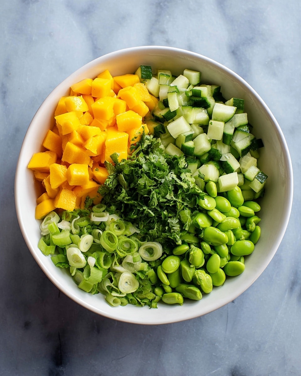 A white bowl sits on a white marbled surface, filled with four distinct layers of fresh ingredients, each occupying its own section. One layer features bright yellow-orange chopped mango pieces with a smooth texture, positioned at the top left. To the top right, there are chopped cucumber pieces in various shades of green with a crisp texture. The bottom right side holds a layer of vivid green edamame beans with a rounded shape and smooth surface. In the center, a small heap of chopped fresh cilantro adds a leafy texture, with a light to medium green color. The bottom left layer contains sliced green onions, showing a mix of white and light green rings, with a soft and moist look. Photo taken with an iphone --ar 4:5 --v 7