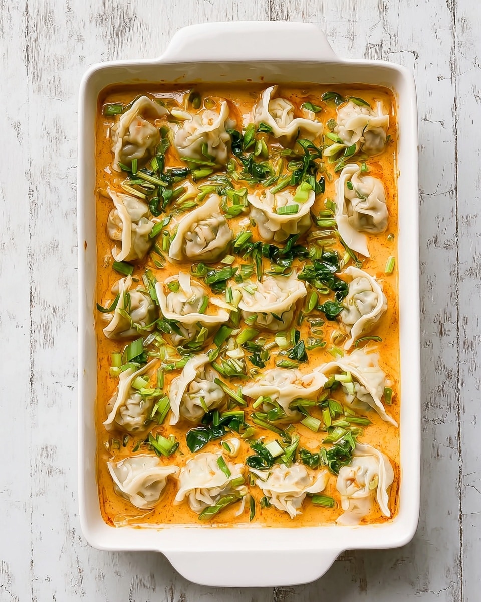 The image shows a white rectangular dish filled with a creamy orange sauce that covers the bottom layer. Scattered evenly on top of the sauce are small dumplings with white, slightly folded, thin wrappers, some partially submerged. Around and between the dumplings are bright green leafy vegetables adding texture and color contrast. The dish sits on a white marbled surface, and the overall view is from above, showing the arrangement clearly. Photo taken with an iphone --ar 4:5 --v 7