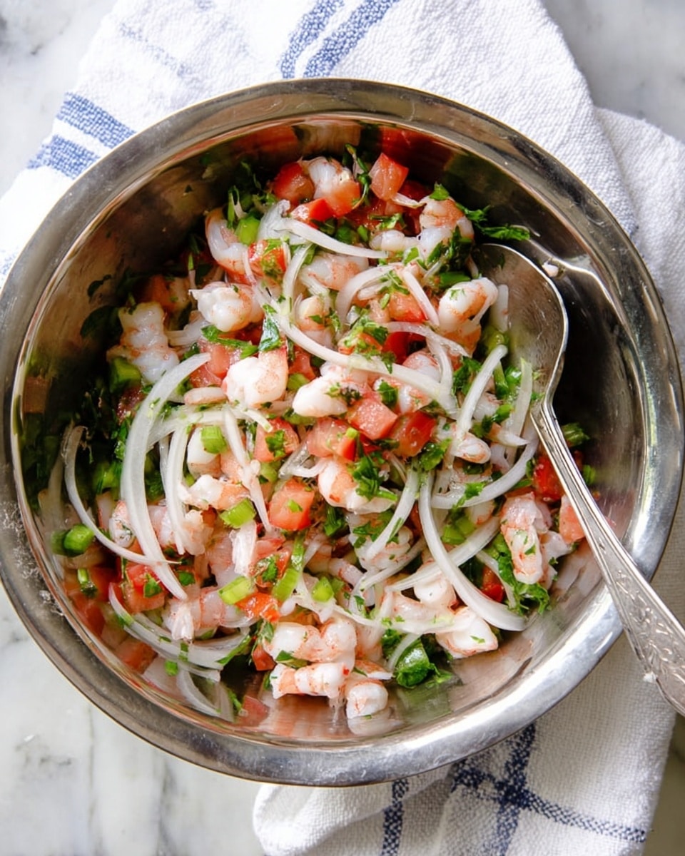 The image shows a shiny silver metal bowl filled with a fresh shrimp salad. The salad has small pieces of pink shrimp mixed with thin white onion slices, green chopped herbs, diced red tomatoes, and small green pepper pieces. A silver spoon is placed inside the bowl, resting on the side. The bowl is set on a white marbled surface, with a white cloth that has light blue stripes partially visible beneath the bowl. Photo taken with an iphone --ar 4:5 --v 7