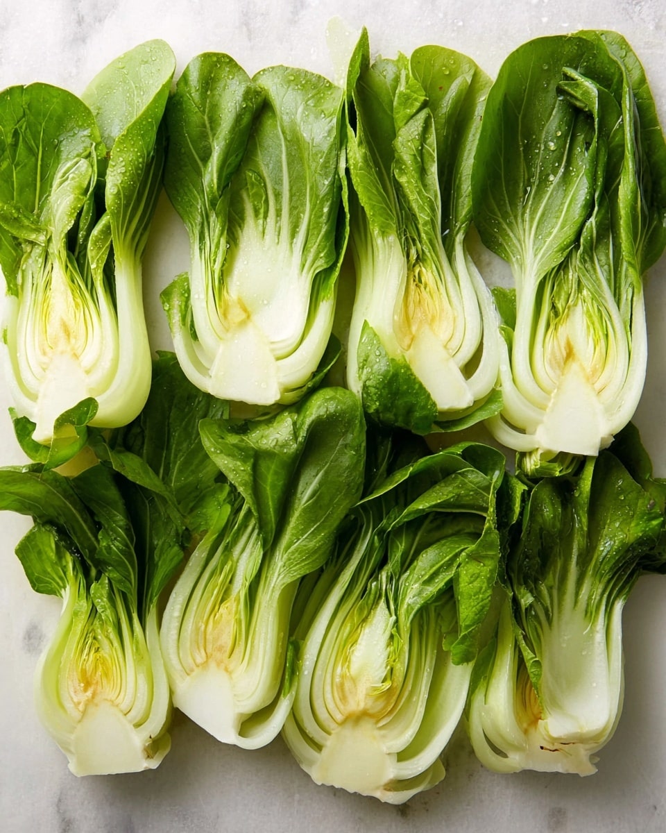 Several halves of fresh bok choy are arranged side by side on a white marbled surface. Each bok choy shows clear layers, with thick white stalks at the base that smoothly curve upward into bright green, slightly wrinkled leaves. The texture shifts from firm and smooth at the bottom to soft and leafy at the top. The layers within the stalks are tightly packed and visible, with some light green and yellow hints nearer the center. The light highlights the natural shine and freshness of the vegetable, showing drops of moisture on the surface. Photo taken with an iphone --ar 4:5 --v 7