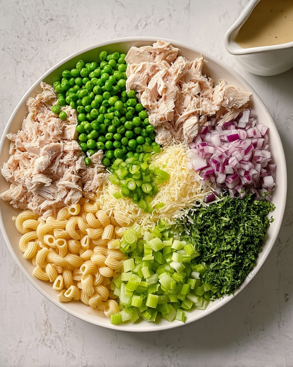 A white bowl sits on a white marbled surface, filled with seven distinct layers of ingredients arranged neatly side by side. Starting from the top left, there is a pile of shredded light beige cooked chicken, followed by a cluster of bright green peas. To the right of the peas, finely chopped purple onions create a colorful patch. Below the onions, a small mound of light green sliced scallions rests next to a heap of finely grated pale yellow cheese. At the bottom, there is a layer of pale yellow macaroni pasta slightly curving around the bowl's edge. Next to the macaroni, vibrant green sliced celery pieces lie below a small section of finely chopped dark green fresh herbs. Off to the side of the bowl, a small white pitcher with a beige sauce is partially visible. The photo taken with an iphone --ar 4:5 --v 7