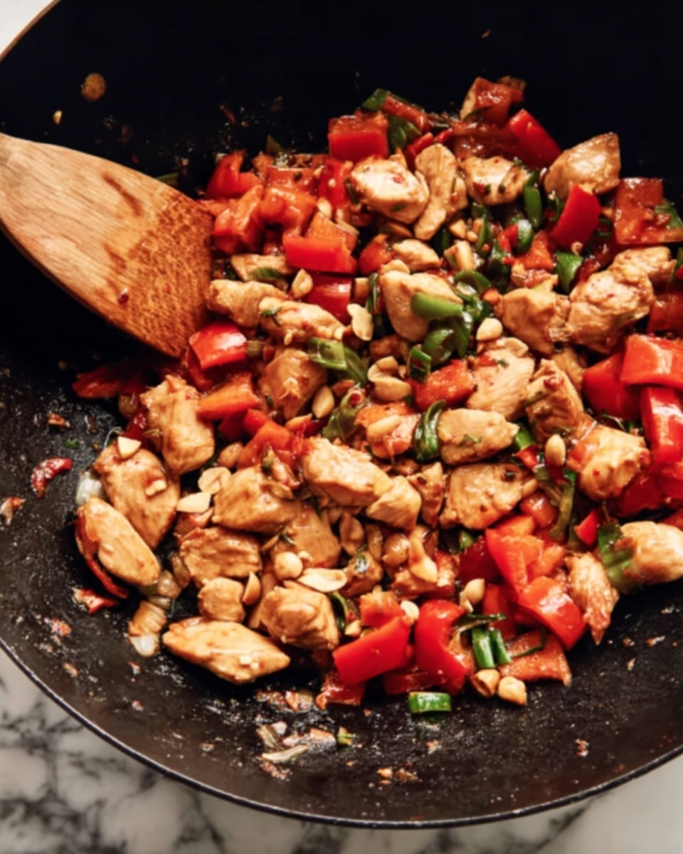The image shows a black wok filled with a colorful stir-fry dish. The dish has three main layers: large pieces of light brown cooked chicken with a slightly shiny texture, bright red chunks of bell pepper scattered evenly, and small green scallion pieces mixed throughout. There are also light tan peanuts sprinkled on top, adding a crunchy texture. A wooden spatula is partially visible on the left side, stirring the ingredients. The background features a white marbled surface photo taken with an iphone --ar 4:5 --v 7