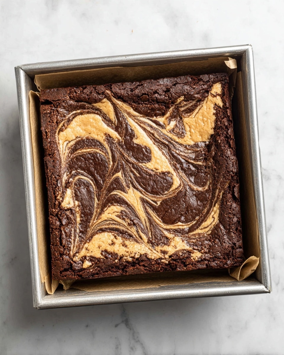 A square baked brownie in a silver baking pan lined with parchment paper, featuring a two-layer design. The bottom layer is deep dark brown, dense and rich in texture. The top layer is a lighter creamy tan swirled with the dark chocolate color in a marbled pattern covering the entire surface. The edges have a slightly raised, cracked crust in dark brown, framing the marbled top. The tray rests on a white marbled surface. Photo taken with an iphone --ar 4:5 --v 7