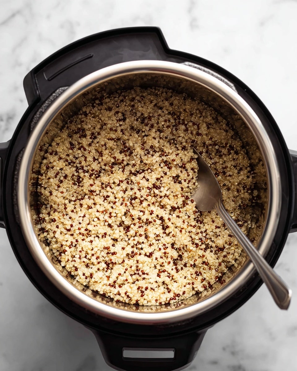 Inside a shiny silver inner pot of a black electric pressure cooker, there is a layer of cooked quinoa with a mix of light beige and small dark red grains, showing a soft, fluffy texture. A silver fork stands upright in the quinoa near the right side of the pot. The pot is placed on a white marbled surface visible below the cooker. photo taken with an iphone --ar 4:5 --v 7