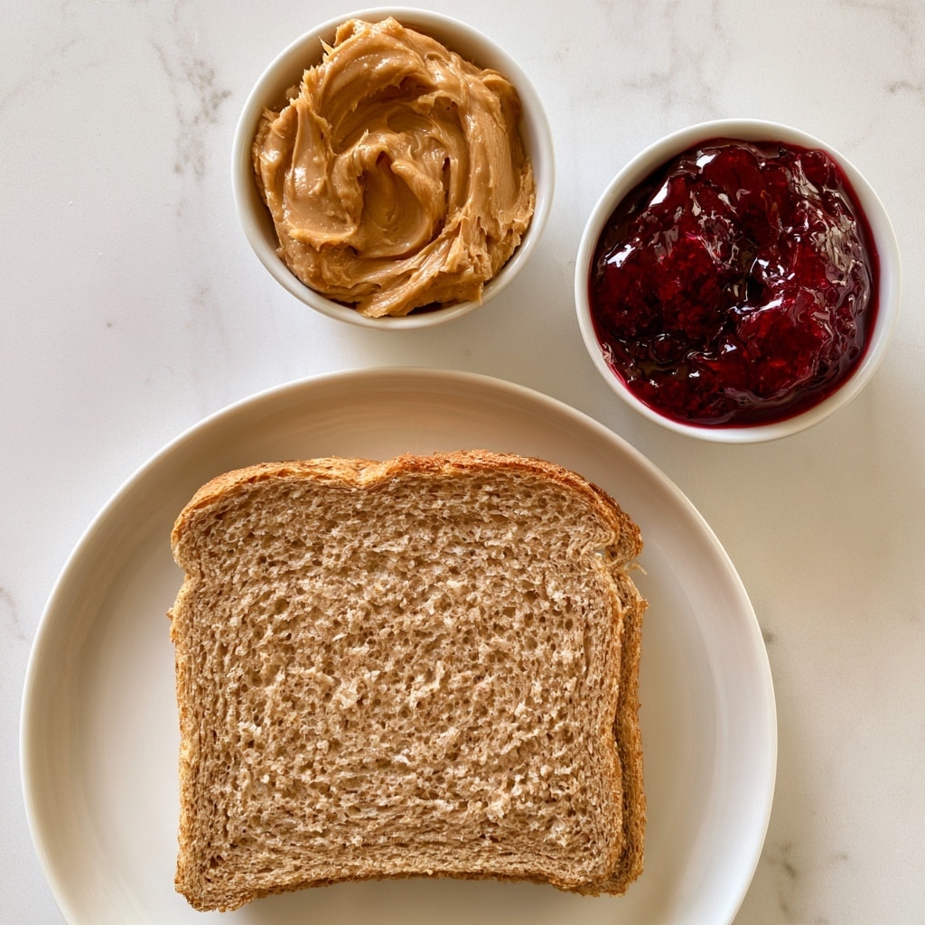 The image shows two slices of brown whole wheat bread stacked on a white plate with a soft texture and visible grain patterns. Above the plate, there are two small white bowls placed on a white marbled surface. The left bowl is filled with creamy, smooth light brown peanut butter, while the right bowl holds shiny, deep red jelly or jam with a slightly chunky texture. The setup is clean and bright with a simple and fresh look, photo taken with an iphone --ar 4:5 --v 7