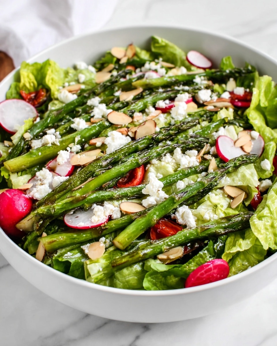 A white bowl filled with a fresh salad featuring several layers: the bottom layer is green lettuce leaves with a ruffled texture, topped with roasted green asparagus spears arranged evenly across the salad; scattered throughout are thin slices of pink radishes and small red tomato pieces, providing pops of color; crumbled white cheese is sprinkled over the top along with thin, light-colored almond slices, adding texture and contrast. The bowl sits on a white marbled surface. photo taken with an iphone --ar 4:5 --v 7