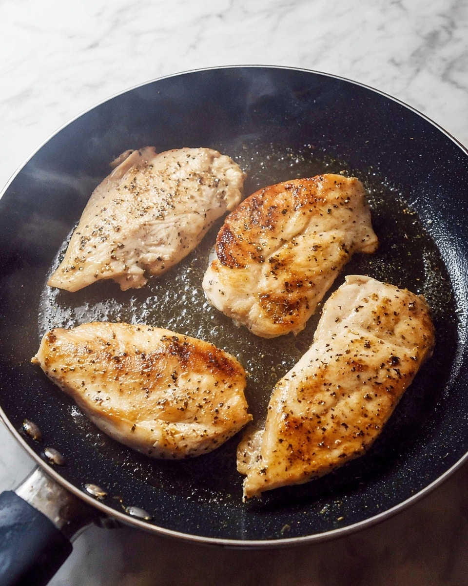 Four pieces of chicken with a light brown color and some black pepper spots are frying in a black pan. The chicken pieces are placed flat, close to each other, and have a cooked outer texture with slight browning on the edges. The pan has small water droplets and steam rising, showing the cooking process. The background is a white marbled surface. photo taken with an iphone --ar 4:5 --v 7