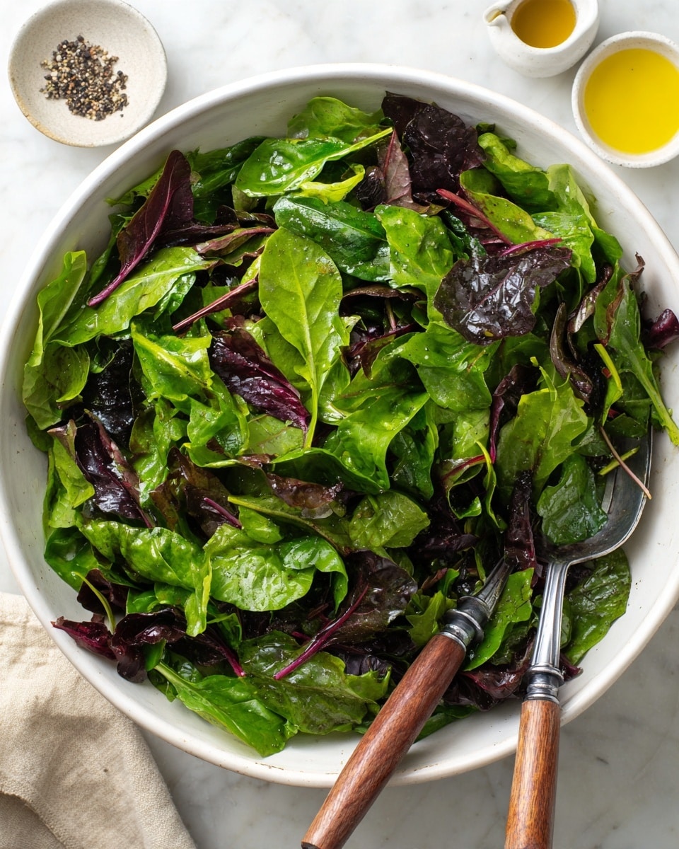 A large white bowl filled with fresh leafy greens including bright green spinach leaves and darker purplish-red leaves mixed together, creating texture and color contrast. Two metal salad forks with wooden handles rest inside the bowl on opposite sides over the greens. Around the bowl, there are small white dishes, one with black pepper and the other with a yellow oil, all placed on a white marbled surface, enhancing the clean, fresh look of the salad. photo taken with an iphone --ar 4:5 --v 7