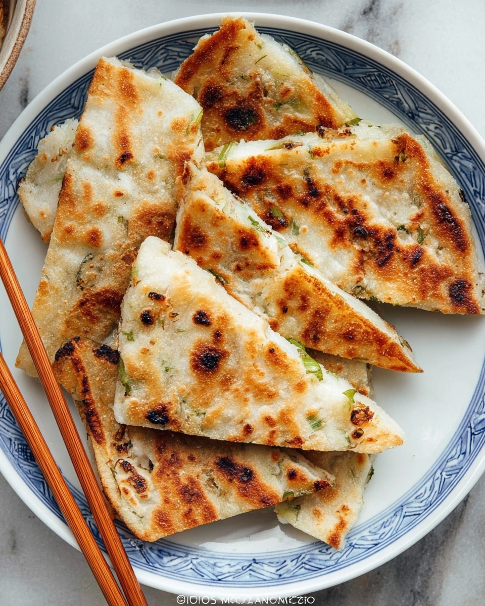 A white plate with a blue rim holds several triangular pieces of golden-brown flatbread with visible charred spots and green onion bits scattered inside the layers, showing a slightly crispy and flaky texture. The flatbread pieces are stacked unevenly, creating a casual arrangement. Wooden chopsticks rest beside the edge of the plate on a white marbled surface. Photo taken with an iphone --ar 4:5 --v 7