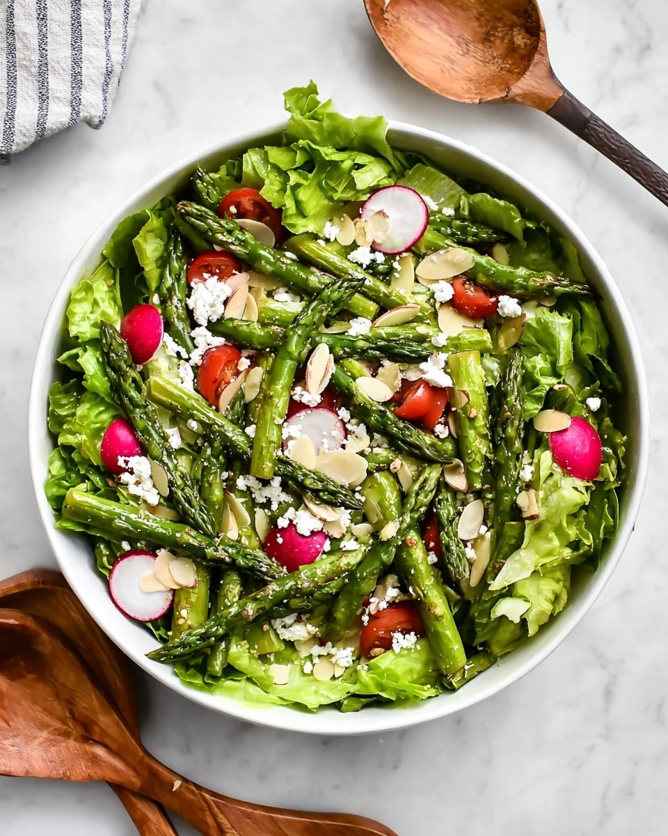 A fresh salad is shown in a white bowl on a white marbled surface. The bottom layer is green leafy lettuce with a ruffled texture. On top of the lettuce, there are bright green asparagus spears laid evenly across the salad. Thin slices of radish, pink with white centers, are scattered throughout. Small, bright red tomato pieces are placed between the other ingredients. Crumbled white cheese is sprinkled over the top, adding a soft, crumbly texture. Thin, pale almond slices are spread lightly over the entire salad. A wooden salad spoon and fork rest beside the bowl. photo taken with an iphone --ar 4:5 --v 7