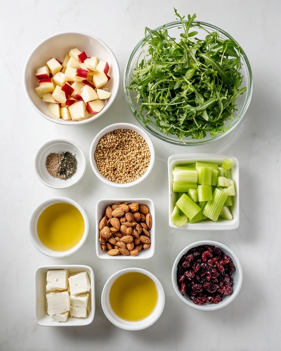 The image shows multiple small white bowls and a large glass bowl on a white marbled surface. The large glass bowl in the top right is filled with fresh green arugula leaves, with their jagged edges and light stems visible. To the left, a medium white bowl contains diced apple pieces with red skin and creamy white flesh. Below that, a smaller white bowl holds sliced green celery with a crisp texture. Another small white bowl nearby contains golden brown wheat kernels. There are two more small white bowls beneath, each holding clear yellow liquids, likely oils or dressings. Below them is a small square white bowl filled with irregular white cheese chunks. Other compartments hold almonds, dried dark red cranberries, whole black pepper, honey, and mustard, each in white bowls or ramekins arranged neatly. The overall setting is clean and bright. photo taken with an iphone --ar 4:5 --v 7