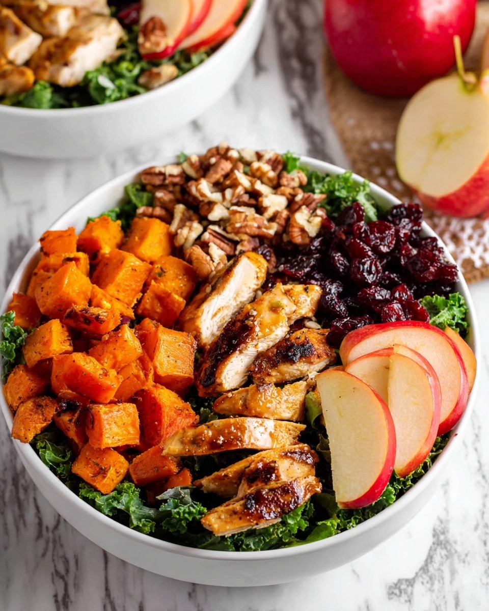 A white bowl filled with several layers starting at the bottom with fresh green leafy kale, topped with golden brown grilled chicken pieces arranged in the middle and left side. To the lower left is a pile of roasted orange sweet potato cubes with a slightly charred texture. On the upper right, there are dark red dried cranberries next to a small pile of chopped light brown nuts. To the right edge, thin, overlapping slices of red and yellow apple are neatly placed. The bowl is set on a white marbled surface with a glimpse of another bowl and apples nearby. photo taken with an iphone --ar 4:5 --v 7