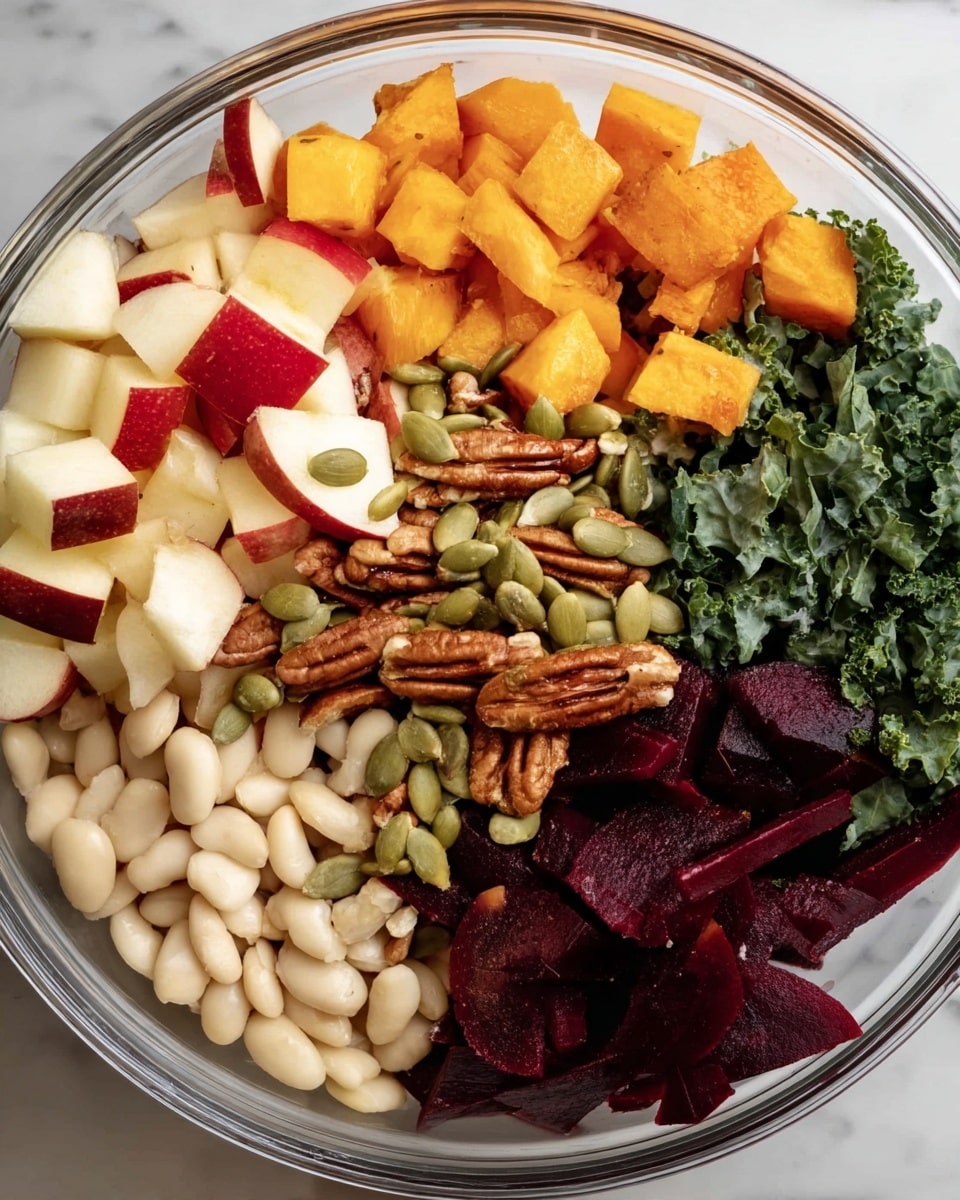 A clear glass bowl contains seven layers of colorful fresh ingredients arranged side by side. On the top left, there are small cubes of red and white apple, bright orange roasted squash chunks are next to the apple. On the top right, there is a small pile of dark green kale leaves. At the bottom left, pale white beans fill a quarter of the bowl, near the bottom center there are thin, dark red beet strips. In the middle, scattered across the center, are pumpkin seeds and whole pecans. The bowl is placed on a white marbled surface photo taken with an iphone --ar 4:5 --v 7