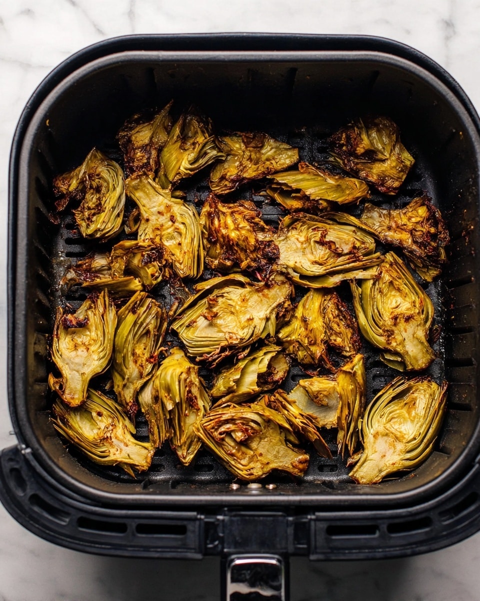 The image shows a single layer of roasted artichoke pieces inside a black air fryer basket. The artichokes are cut into different sizes, some showing the inner layers with a soft yellowish-green color, and others with crispy, slightly browned edges. The texture appears rough and slightly charred in spots, giving a roasted look. The air fryer basket has grill lines visible beneath the artichokes and sits atop a white marbled surface. photo taken with an iphone --ar 4:5 --v 7