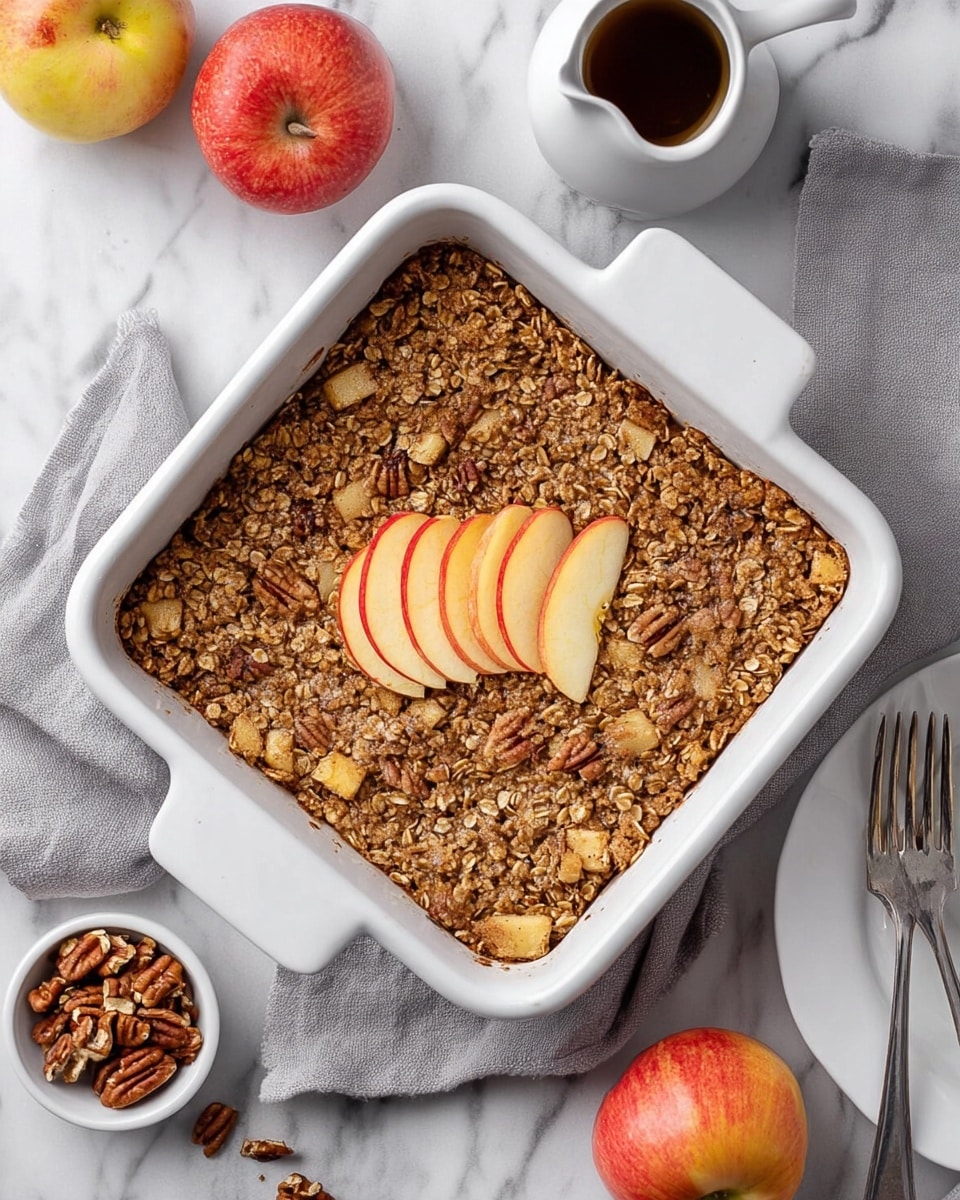 A square white ceramic dish filled with a baked oatmeal mixture that has a rough, crumbly texture with visible chunks of light brown baked apple and pieces of pecans scattered throughout. In the middle of the oatmeal, there are three thin, overlapping slices of apple with red edges and pale yellow centers. The dish is placed on a soft gray cloth on a white marbled surface. Around the dish, there are two whole red and yellow apples, a small white bowl with chopped pecans, a white small pitcher with a dark liquid, and a white plate with a fork and knife. Photo taken with an iphone --ar 4:5 --v 7
