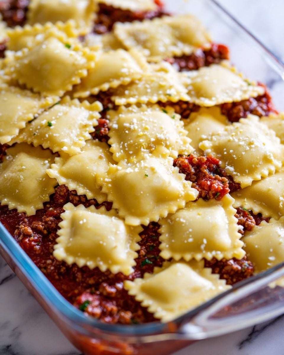 This image shows a close-up of a clear white dish filled with layers of food. The bottom layer is a chunky red sauce with bits of ground meat and small specks of green herbs. On top of this sauce, there is a scattered layer of uncooked square ravioli pasta, pale yellow in color with crinkled edges. The ravioli pieces are stacked unevenly, some overlapping and others standing slightly upright. The background surface is a white marbled texture. photo taken with an iphone --ar 4:5 --v 7