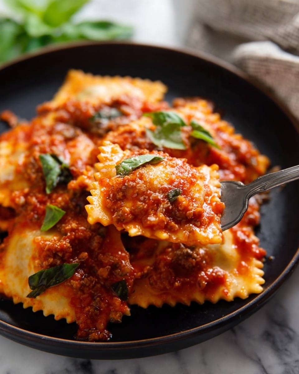 A close-up of a black plate filled with several layers of ravioli pasta covered in thick red tomato sauce mixed with small bits of meat and green basil leaves sprinkled on top. The ravioli are square with slightly wavy edges, and the tomato sauce has a chunky texture, coating the pasta fully and pooling slightly at the bottom. A metal fork is lifting a small piece of ravioli topped with sauce near the right side of the plate. The background shows a white marbled texture under the plate and blurred green basil leaves in the corner. photo taken with an iphone --ar 4:5 --v 7